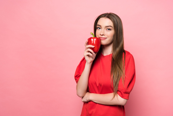 smiling attractive young woman holding red bell pepper and looking at camera on pink - Foto, imagen
