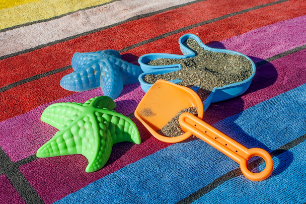 Juguetes de arena en una toalla de playa colorida
 - Foto, Imagen