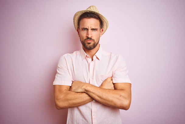 Красивый мужчина в шляпе и летней рубашке на розовом изолированном фоне скептически и нервно, неодобрительное выражение лица со скрещенными руками. Отрицательное лицо
. - Фото, изображение