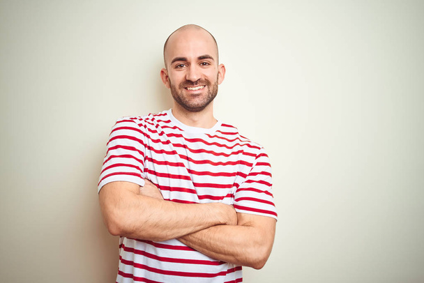 Jonge kale man met baard dragen casual gestreepte rode t-shirt over witte geïsoleerde achtergrond gelukkig gezicht glimlachend met gekruiste armen kijken naar de camera. Positieve persoon. - Foto, afbeelding