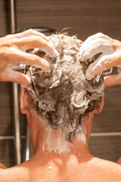 Hombre espalda espuma su champú mientras se lava el pelo en la ducha
 - Foto, imagen