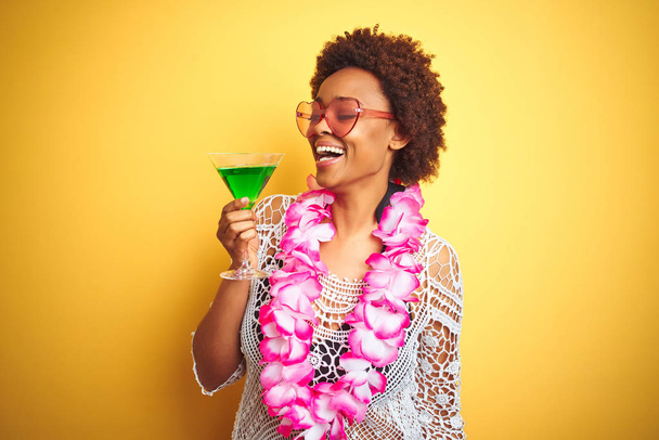 Giovane donna afro-americana con i capelli afro indossa fiori hawaiani lei e bere un cocktail con un viso felice in piedi e sorridente con un sorriso fiducioso mostrando denti
 - Foto, immagini