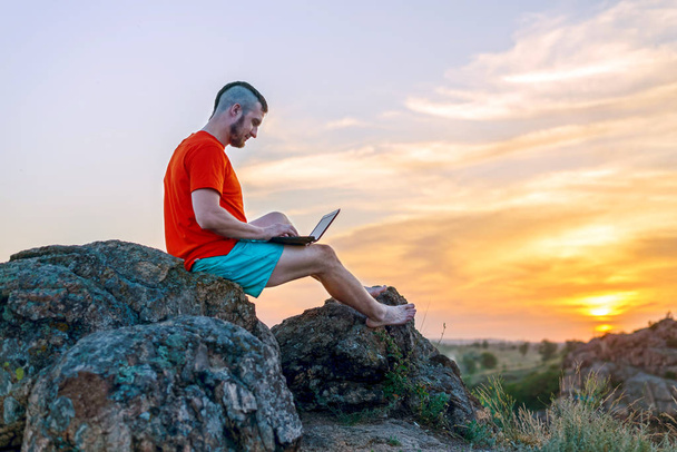 Business man working on a laptop while sitting on a rock, free space. - Zdjęcie, obraz