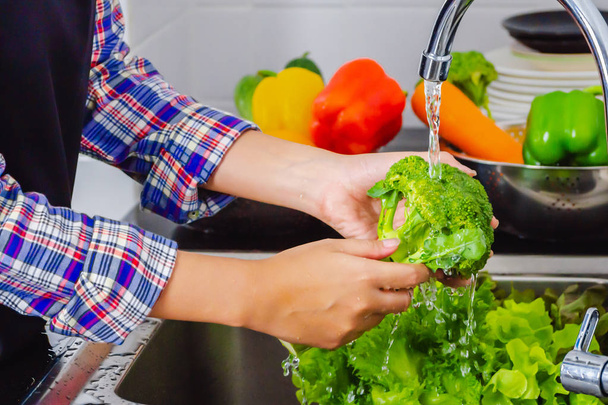 Jonge vrouw wassen broccoli om pesticiden te verwijderen voor het koken in de keuken. Concept voor het wassen van groenten en fruit. - Foto, afbeelding