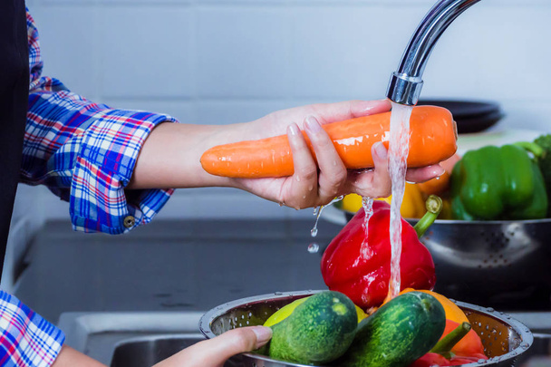 Young woman washing carrot to remove pesticides before cooking in kitchen. Fruit and vegetables washing concept. - Foto, Imagen