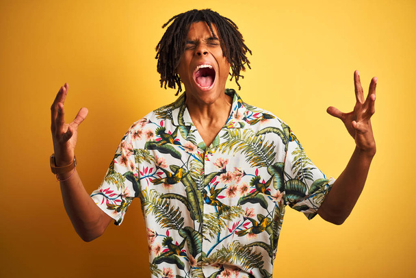 Hombre afro con rastas de vacaciones con camisa de verano sobre fondo amarillo aislado celebrando loco y loco por el éxito con los brazos levantados y los ojos cerrados gritando emocionados. Concepto ganador
 - Foto, imagen