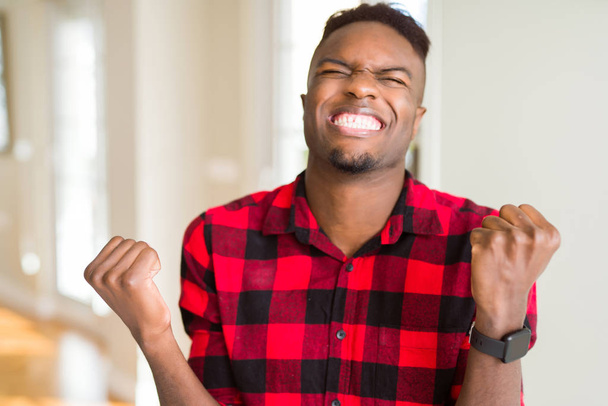 Pohledný afroamerický muž velmi šťastný a vzrušený s vítězným gestem se zdviženýma rukama, usmívaje se a křičí na úspěch. Koncepce oslav. - Fotografie, Obrázek