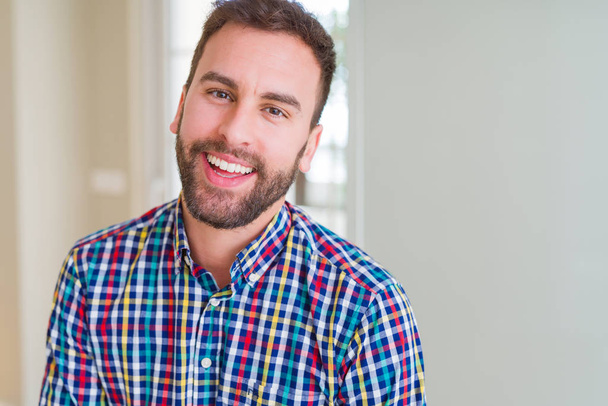 Όμορφος άνδρας φορώντας πολύχρωμο πουκάμισο και χαμογελαστός θετικά στο το  - Φωτογραφία, εικόνα