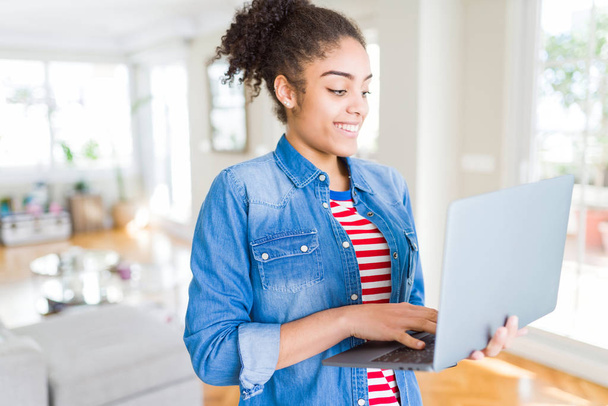 Young african american girl standing working using laptop with a happy face standing and smiling with a confident smile showing teeth - Fotó, kép