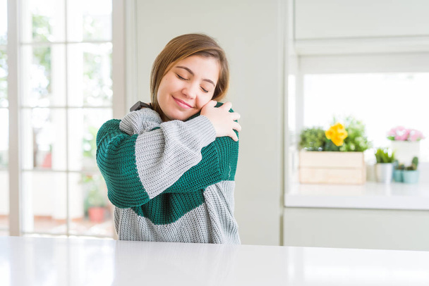 Молодая красивая женщина plus size в случайном полосатом свитере обнимает себя, счастлива и позитивна, улыбается уверенно. Самолюбие и забота о себе
 - Фото, изображение