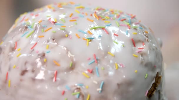 Close up top view of Easter traditional pastry with white glaze and sweet colorful confetti on blurred background, orthodox holidays. Stock footage. Bakery decoration background - Footage, Video