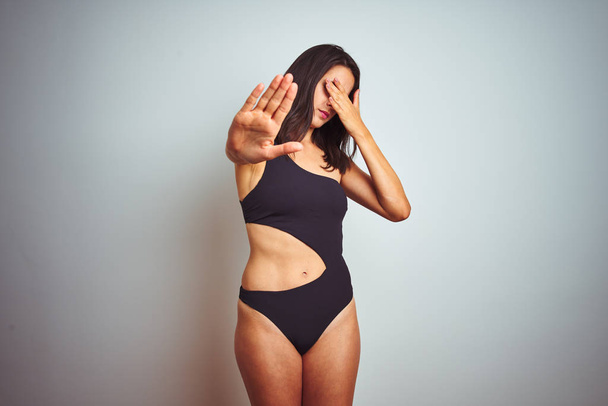 Beautiful woman wearing bikini swimwear over white isolated background covering eyes with hands and doing stop gesture with sad and fear expression. Embarrassed and negative concept. - Фото, зображення