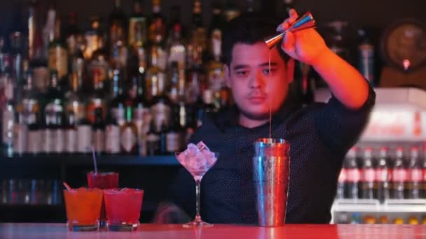 Genç profesyonel barmen bir ölçüm cam ile bir shaker içine portakal şurubu dökün ve bir kaşıkla karıştırın. - Video, Çekim