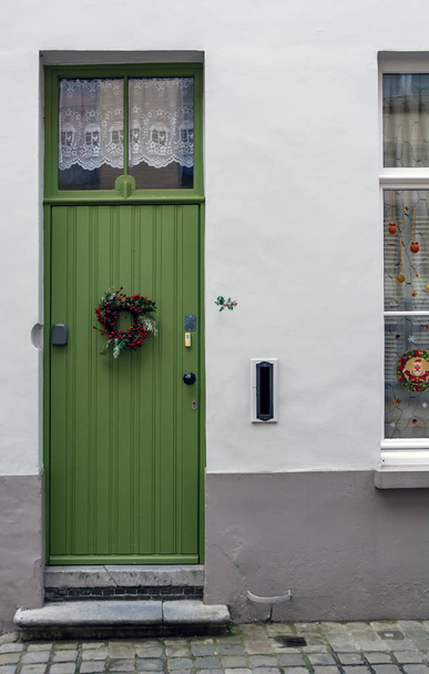 ベルギーのブルージュで撮影されたクリスマスリースで飾られたヴィンテージグリーンの正面玄関。上部に窓が付いている古い緑色のドア. - 写真・画像