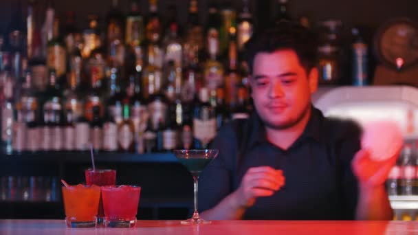 O empregado de bar profissional jovem põe um copo com um coquetel azul em um guardanapo e dá-o para a frente
 - Filmagem, Vídeo