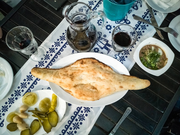Bread. Traditional freshly baked bread lies on a white plate on a dark wooden table. Authentic Georgian bread, red wine and snacks. White linen napkin with national pattern. Gourmet Luxury European. - 写真・画像