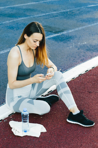 Giovane donna seduta a terra con una bottiglia d'acqua dopo aver fatto jogging all'aperto
 - Foto, immagini