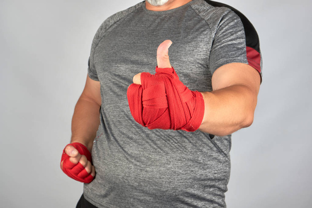 τα χέρια του αθλητή τυλιγμένο σε κόκκινο ελαστικό αθλητικό επίδεσμο δείχνουν ένα l - Φωτογραφία, εικόνα