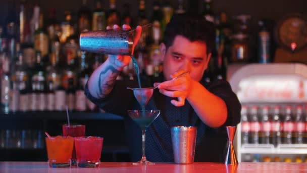 Jovem barman profissional derrama licor azul em um copo usando uma peneira
 - Filmagem, Vídeo