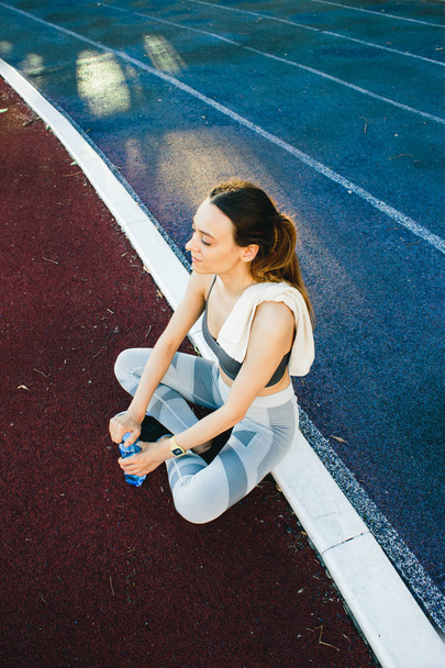 Bella donna seduta a terra con una bottiglia d'acqua dopo aver fatto jogging all'aperto
 - Foto, immagini