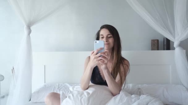 a young woman in underwear in her bed using her mobile phone - Video, Çekim