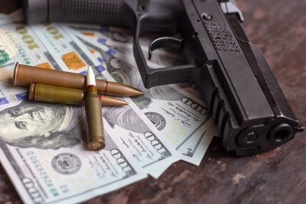 Black gun and weapon bullets on American dollars background. Military industry, war, global arms trade and crime concept. - Photo, Image