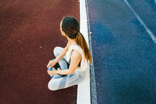 Mujer bonita sentada en el suelo con una botella de agua después de correr al aire libre
 - Foto, imagen