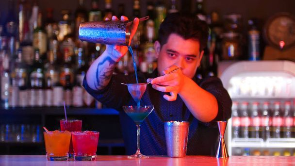 Nuori baarimikko kaataa cocktailin lasiin ravistimesta käyttäen seulaa
 - Valokuva, kuva