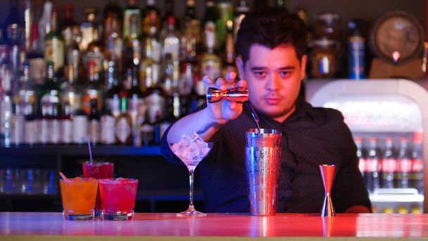 Giovane barista in piedi davanti ai suoi dispositivi barista versando uno sciroppo nello shaker un bicchiere con ghiaccio cocktail sul banco
 - Foto, immagini