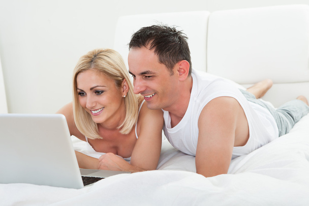 Happy Couple Lying On Bed Using Laptop - Photo, image
