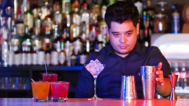Молодий професійний бармен стоїть перед своїми барменними пристроями склянка з льодом - коктейлі на підставці
 - Фото, зображення