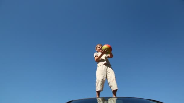 Boy stands on roof of car and throws up ball - Video, Çekim