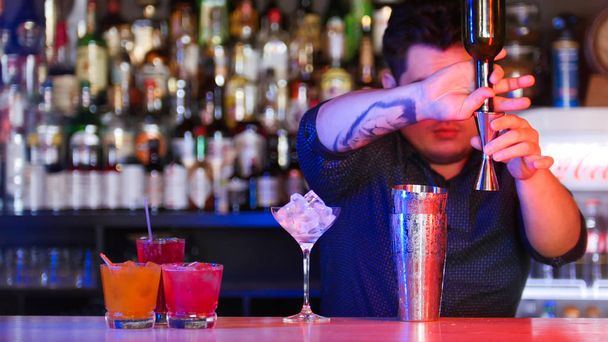 Giovane barista in piedi davanti ai suoi dispositivi barista versando uno sciroppo nel misurino un bicchiere con ghiaccio cocktail sul banco
 - Foto, immagini
