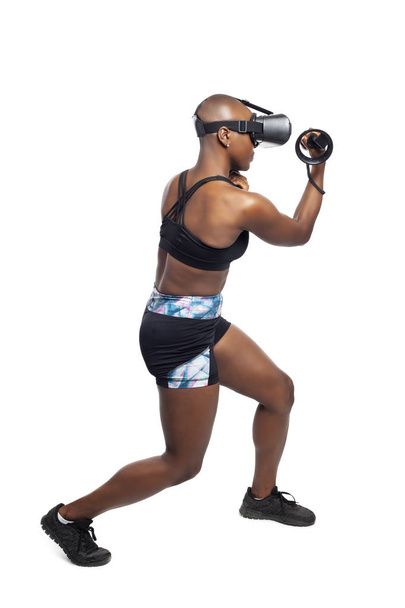 Athletic black female gamer playing video games and exercising while wearing a virtual reality headset.  She is punching like she is boxing or fighting.  Depicts wearable technology and healthy activities.  - Photo, image