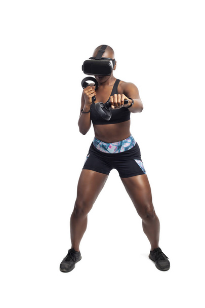 Athletic black female gamer playing video games and exercising while wearing a virtual reality headset.  She is punching like she is boxing or fighting.  Depicts wearable technology and healthy activities.  - Foto, afbeelding