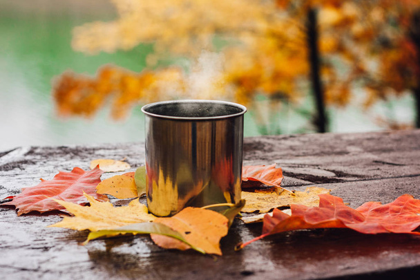 Hot drink in the steel cup on the wooden table. Autumn orange leaves. - Fotografie, Obrázek