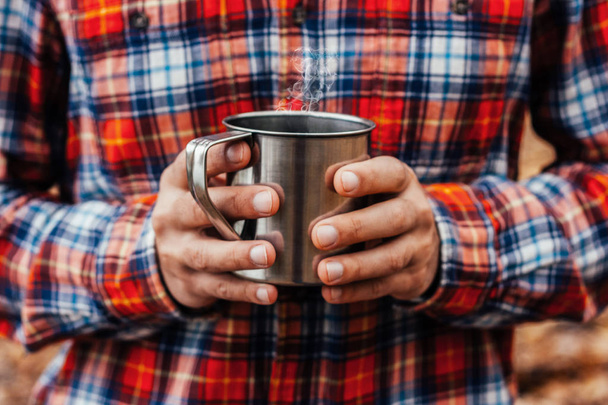 Steel cup with a hot drink in man's hands in the autumn park - Фото, зображення