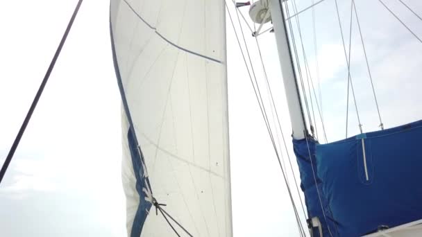 Fehér vitorlák röpködnek a szél mozgó vitorlás jacht hátterében kék ég a tengeri utazás során. Yachting, mint relaxációs aktív életmód. - Felvétel, videó