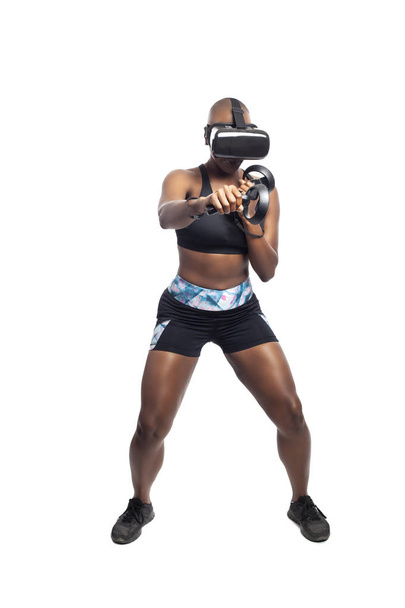 Athletic black female gamer playing video games and exercising while wearing a virtual reality headset.  She is punching like she is boxing or fighting.  Depicts wearable technology and healthy activities.  - Zdjęcie, obraz