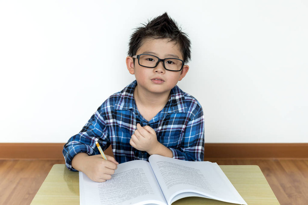 Маленький студент в очках делает домашнюю работу на столе
 - Фото, изображение