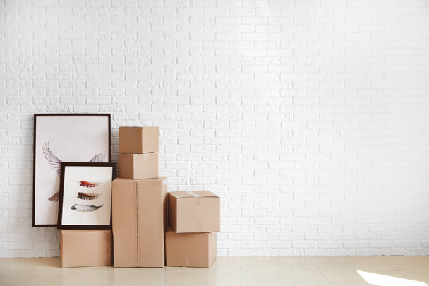 Cajas de cartón con pertenencias preparadas para mudarse a una casa nueva cerca de la pared de ladrillo blanco
 - Foto, Imagen