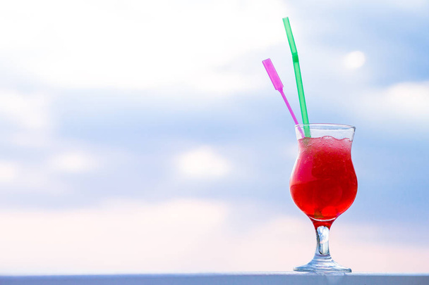 Tasty red cocktail with ice in the glass with a straw on the edge of the pool. - 写真・画像