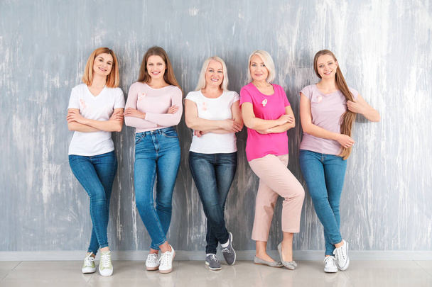 Hermosas mujeres de diferentes edades con cintas rosadas cerca de la pared gris. Concepto de cáncer de mama
 - Foto, imagen
