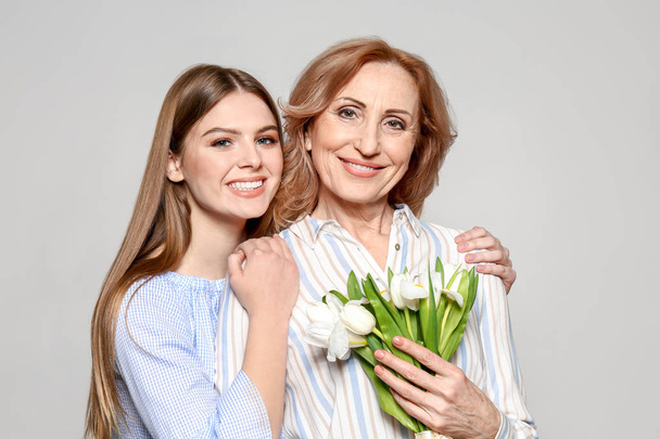 Portrait of mother and her daughter with bouquet on light background - Photo, Image