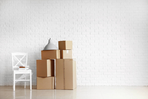 Scatole di cartone con oggetti preparati per trasferirsi in una nuova casa vicino al muro di mattoni bianchi
 - Foto, immagini