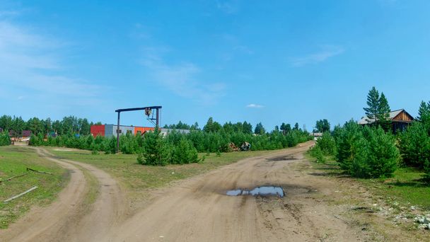 Вилка дороги к жилым сельским домам и рабочей зоне в северной деревне Якутия на фоне еловой лесной тундры
. - Фото, изображение