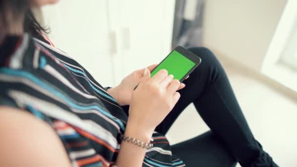 Hermosa chica sosteniendo un teléfono inteligente en las manos con una pantalla verde
 - Metraje, vídeo
