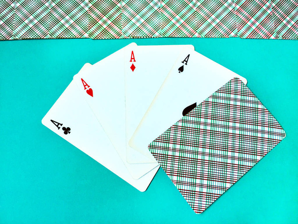 eine gewinnende Pokerhand aus vier Assen alter Spielkarten unterschiedlicher Farbe und einer umgedrehten Karte mit ihnen auf blauem Hintergrund. oberste Reihe invertiert geschlossener Spielkarten. Ansicht von oben, Nahaufnahme. - Foto, Bild
