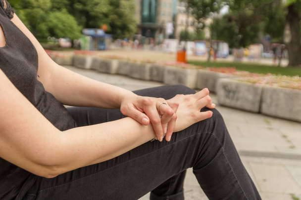Una mujer joven con artritis reumatoide descansa sentada en un banco en un patio de un hospital. Las manos y las piernas están deformadas. Siente dolor. Enfoque seleccionado
. - Foto, imagen