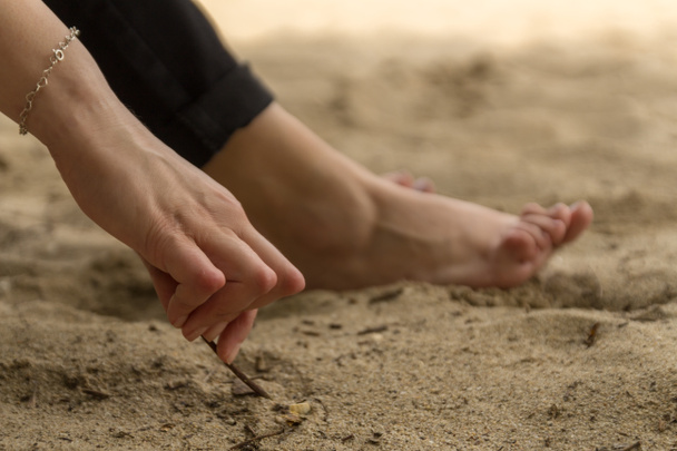 Jonge vrouw met reumatoïde artritis neemt een rust zittend op het zand in de buurt van het strand. Handen en benen zijn vervormd. Ze voelt pijn. Geselecteerde focus. - Foto, afbeelding
